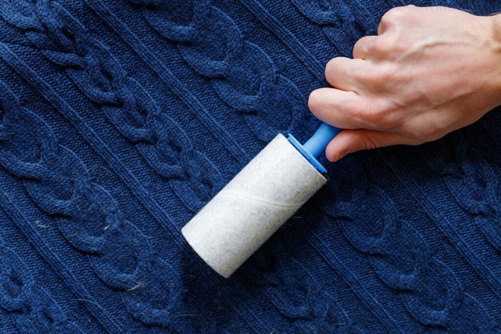 A hand uses a lint roller on a dark blue, cable-knit fabric to remove lint or pet hair.