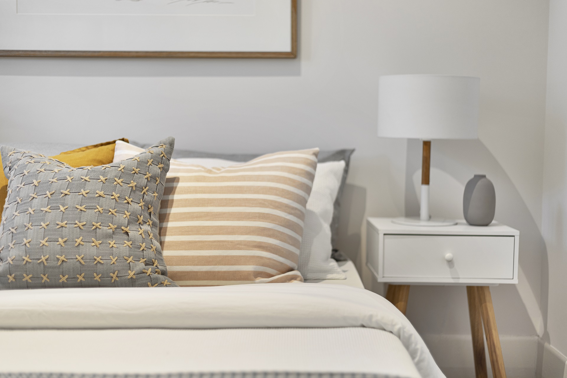 A bed with striped and patterned pillows next to a white nightstand with a lamp and small decorative object.